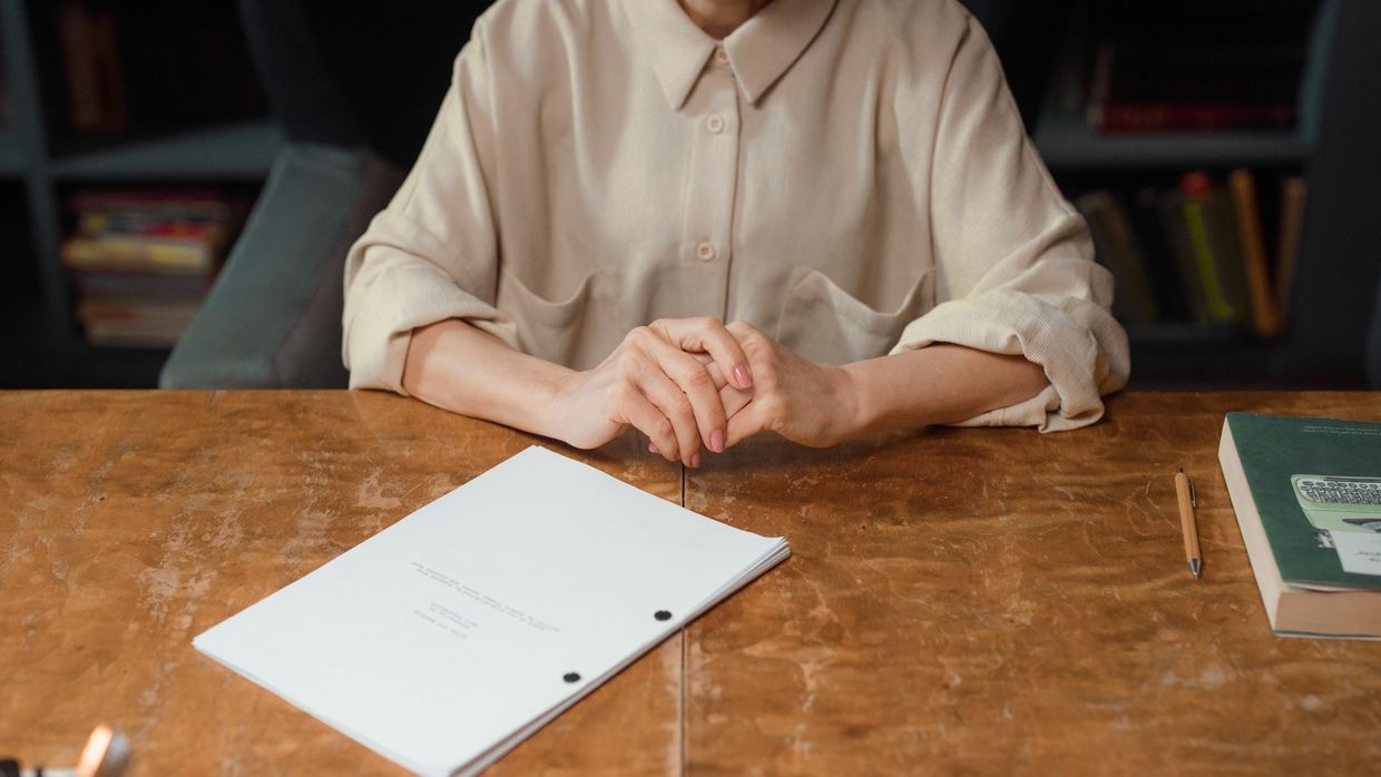 This site: woman sitting at wooden desk reviewing a screenplay in an office setting