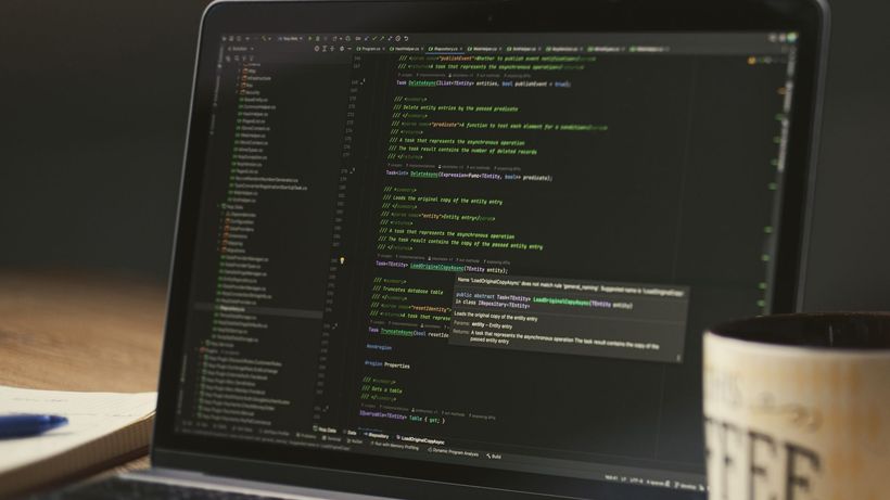 A close-up of a laptop displaying code in a dimly lit room with a coffee mug nearby
