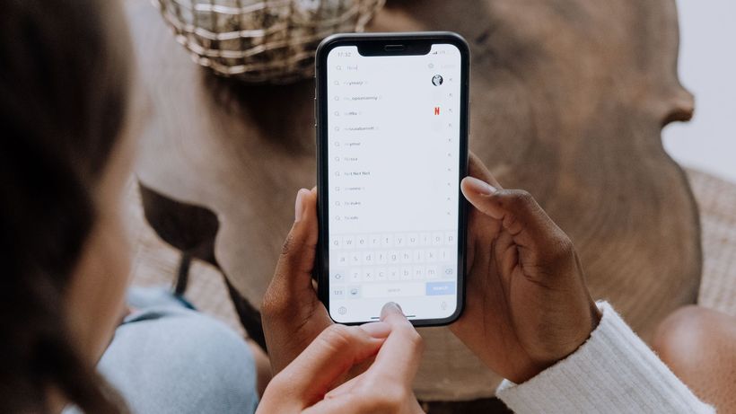 Close-up of hands holding a smartphone, searching for apps like TikTok on a wooden table