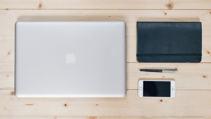 A clean, organized desk featuring a laptop, smartphone, notebook, and pen, ideal for productivity