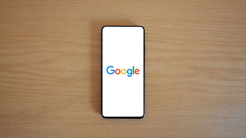A smartphone displaying the Google homepage on a wooden surface, viewed from above