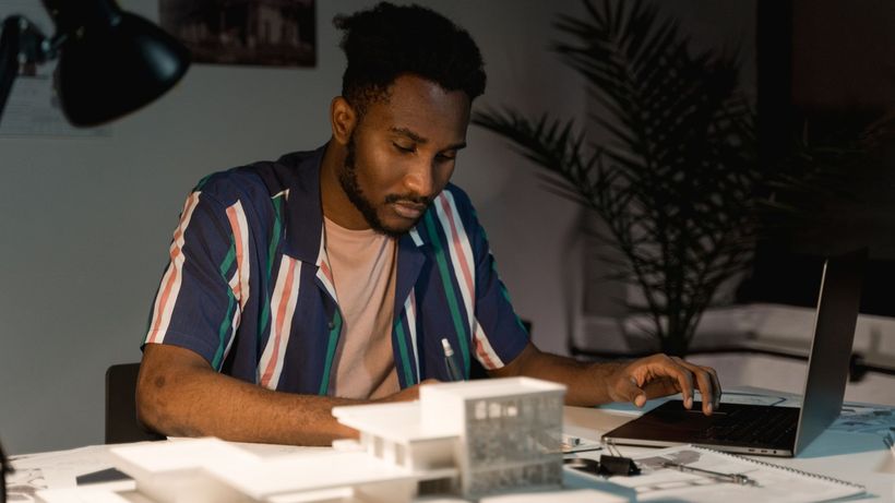 An architect working late at night in an office, using a laptop and surrounded by building models