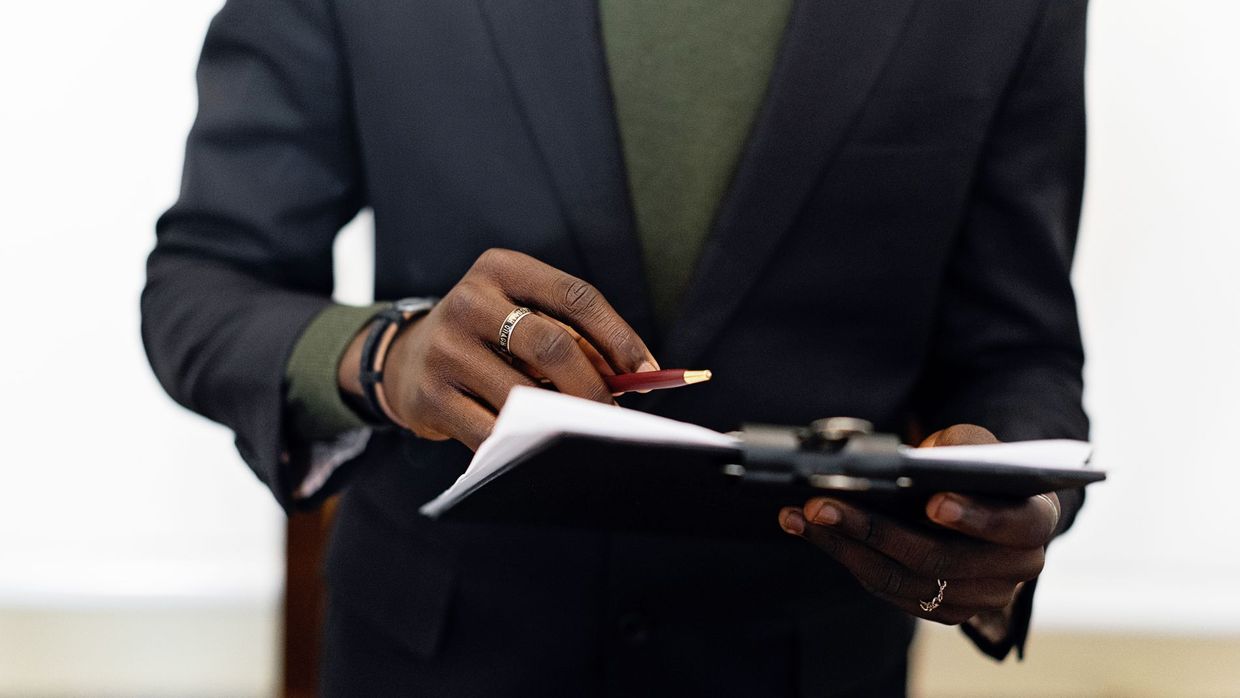 Content audits: close-up of an adult in a blazer holding a clipboard with documents and a pen indoors