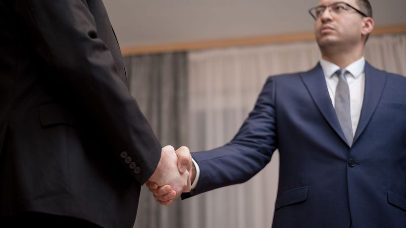 Two businessmen in formal attire shaking hands during a meeting