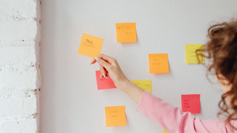 Woman organizing tasks using sticky notes on a wall, promoting productivity and planning
