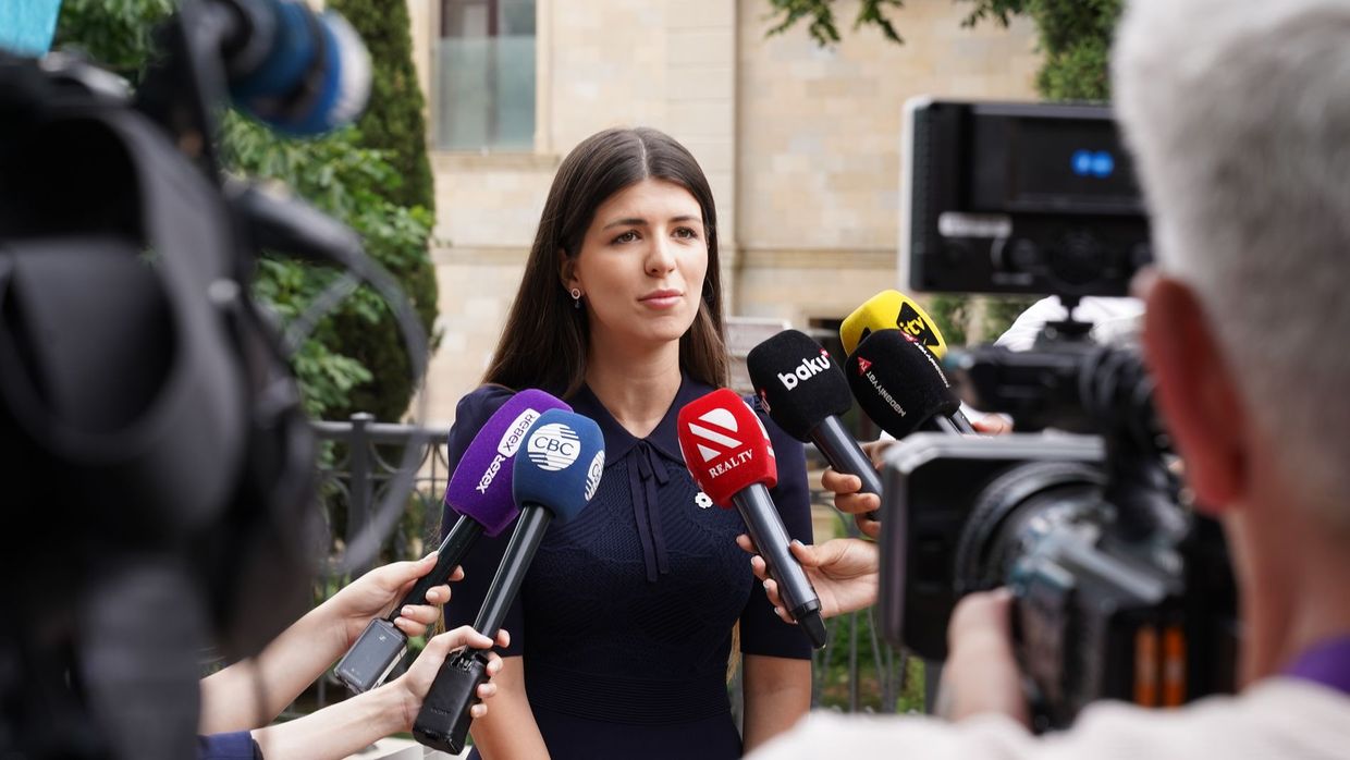 Editorial standards: a spokesperson engages with media during an outdoor press interview surrounded by microphones