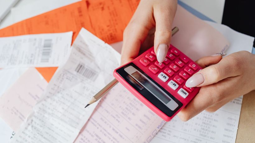 Hands using a pink calculator to manage expenses amidst various receipts and documents