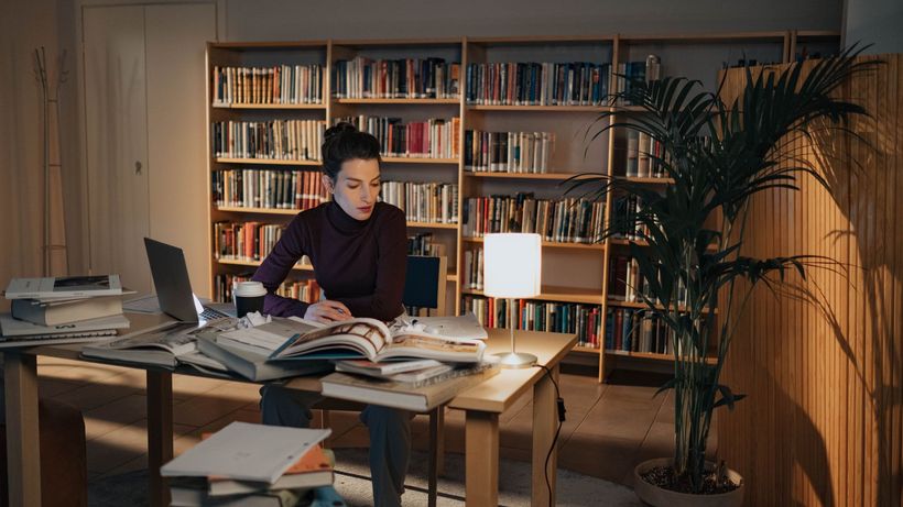 A dedicated student studying late at night in a library setting, surrounded by books
