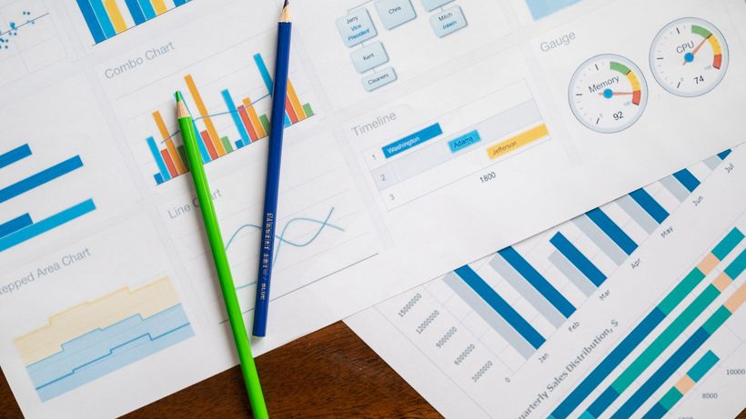 Flat lay of various business charts and colored pencils on wooden table, highlighting financial analysis