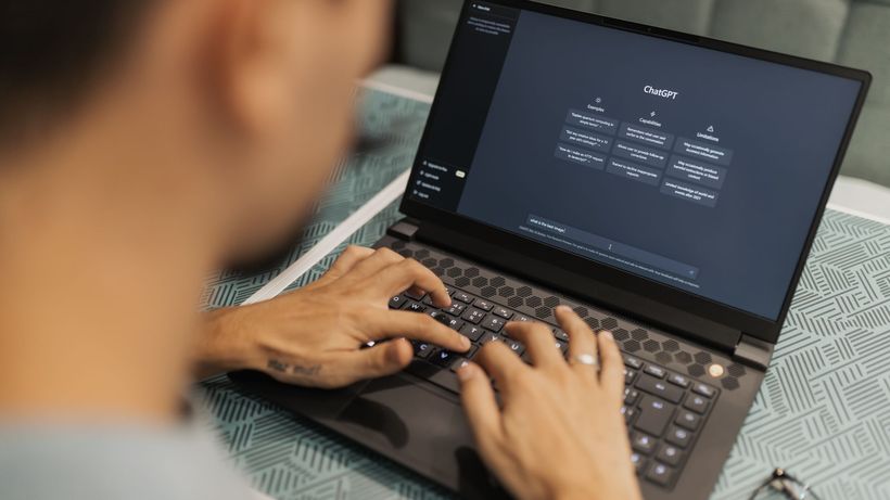 A focused individual types on a laptop running AI software indoors