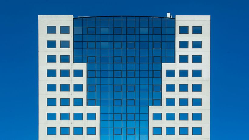 A modern office building featuring a striking geometric facade against a clear blue sky