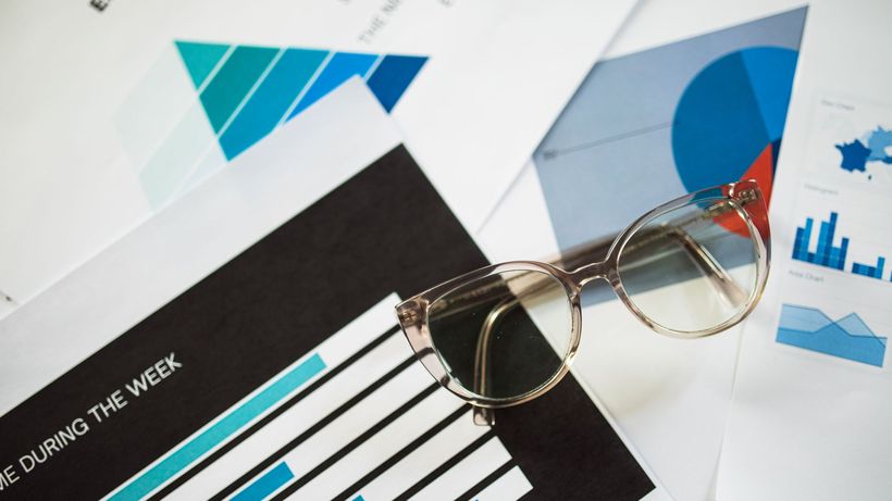 Close-up of eyeglasses resting on financial documents with various charts and graphs
