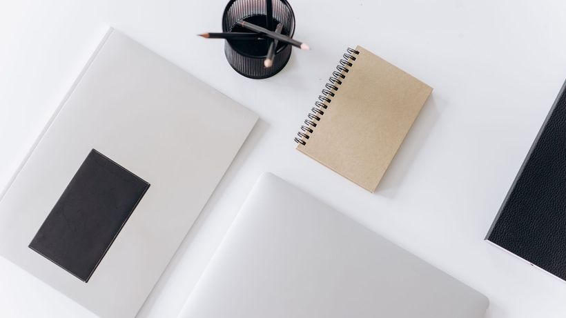 Top view of modern laptop with notebooks and cup of pencils composed on white table in office