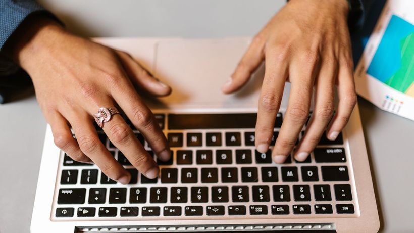 Hands typing on a laptop with a ring, emphasizing technology and work