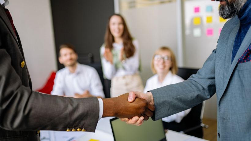 Close-up of a handshake between colleagues in a professional office setting, emphasizing teamwork and agreement