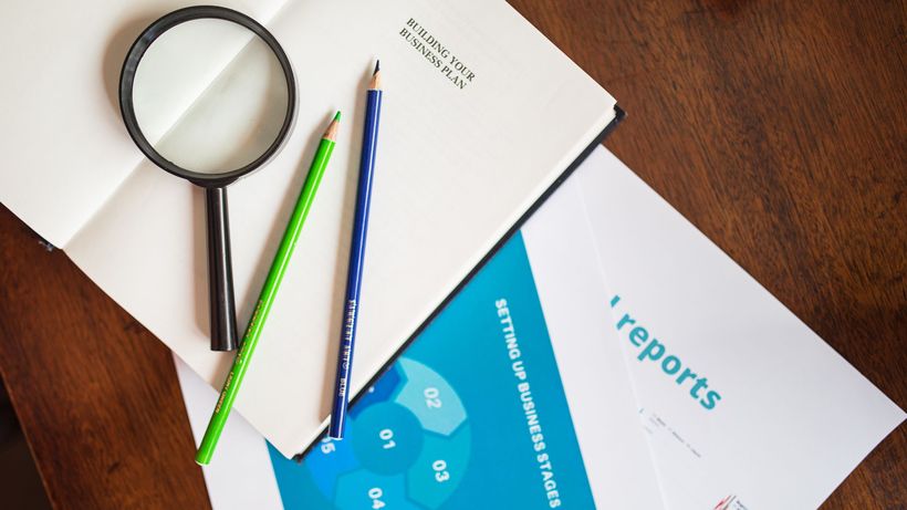 A top view of a magnifying glass, colored pencils, and business reports on a wooden table