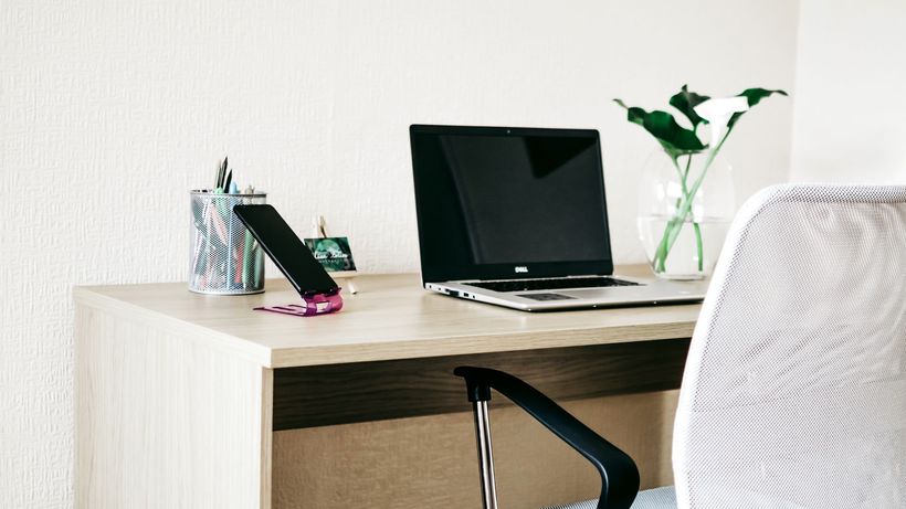 A clean and modern home office workspace with a laptop, smartphone, and plant on a wooden desk