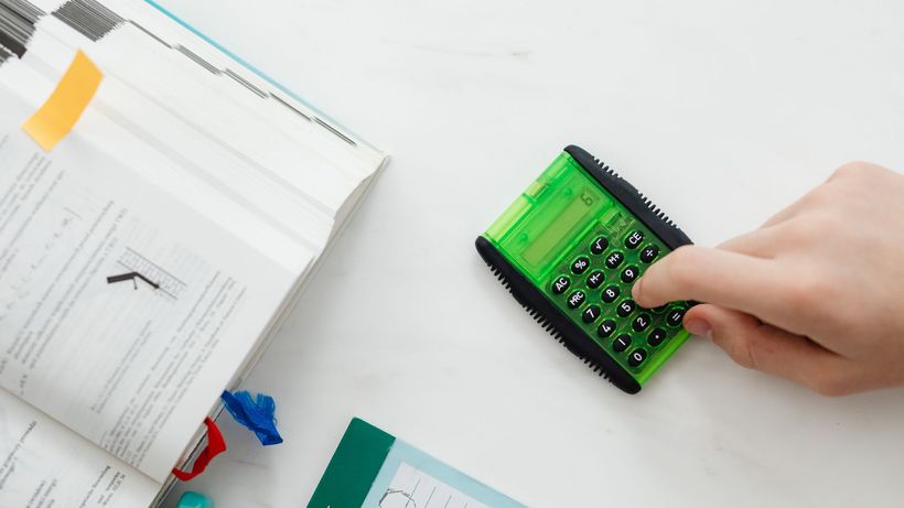 A student uses a green calculator to solve math equations from a textbook on a desk