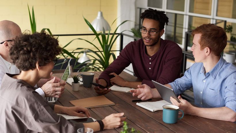 A diverse group of colleagues brainstorming at a wooden table in a modern indoor office setting