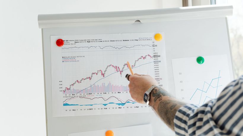 A tattooed person pointing at finance charts and graphs on a whiteboard