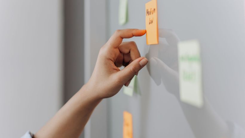 A hand placing a sticky note on a reflective surface in an office setting