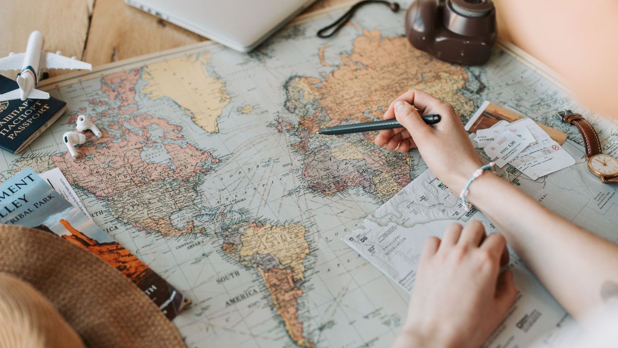 International SEO: hands marking destinations on a world map surrounded by travel essentials like passport and camera