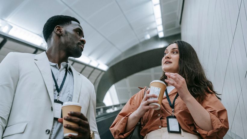 Two business professionals conversing casually on an escalator while holding coffee cups