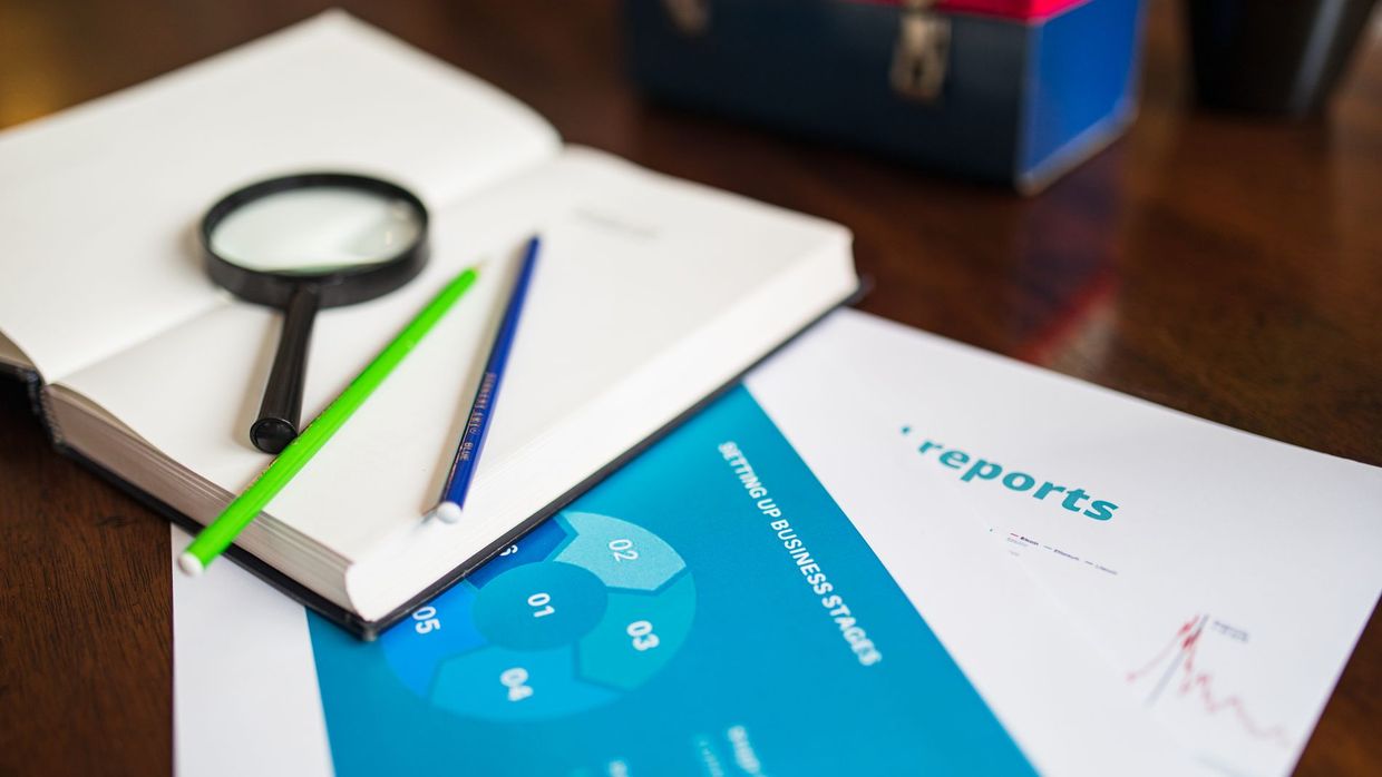Whether SEO is dead: open book with magnifying glass, pencils, and a business report on a wooden desk