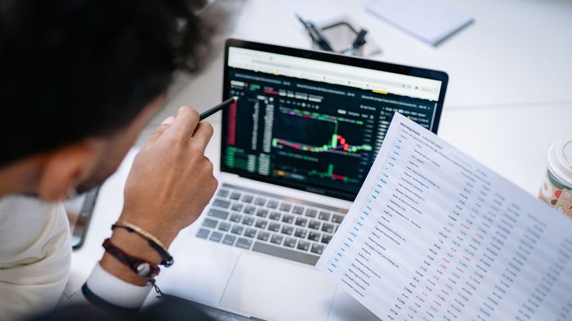 A professional analyzing stock market data on a laptop screen with financial documents