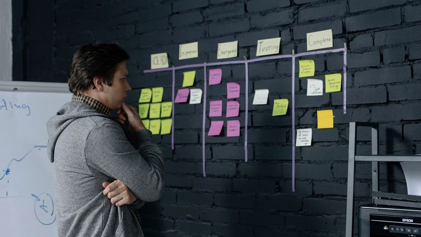 Adult male focusing on task planning using sticky notes on a black wall in a contemporary office setting