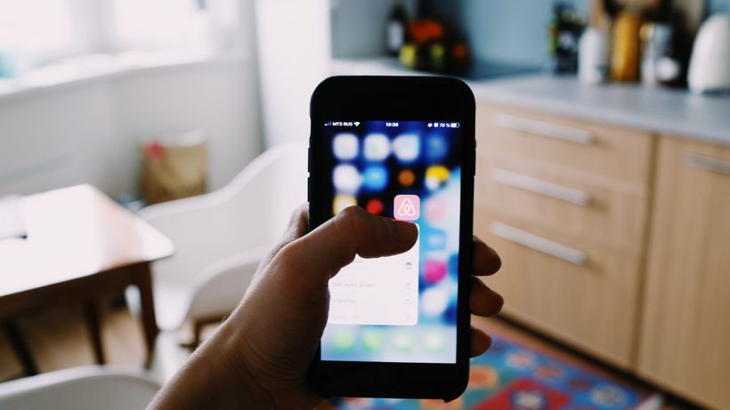 Crop anonymous person demonstrating app touching mobile phone screen while taking gadget with hand in kitchen in apartment