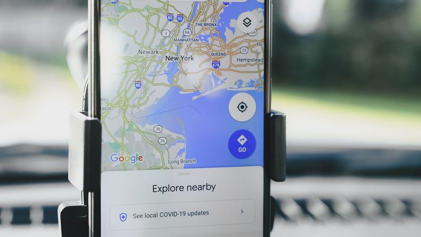 A smartphone displaying GPS map of New York City secured in a car mount during daylight
