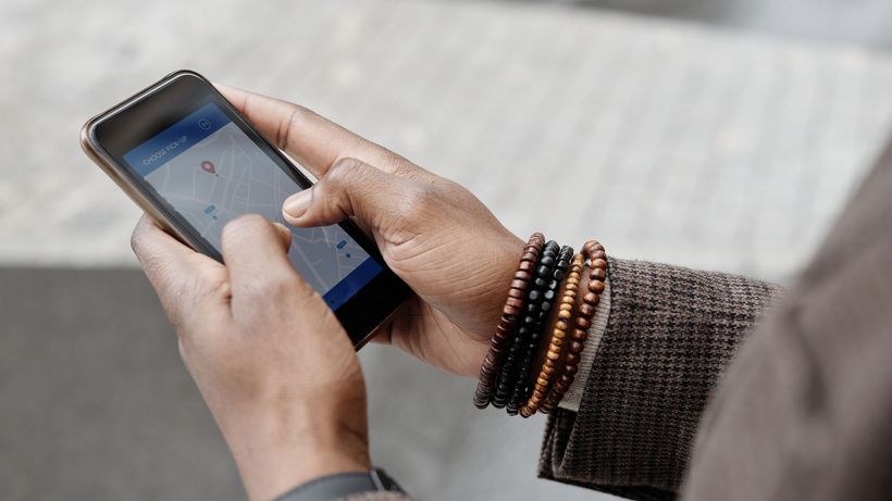 Close-up of hands with bracelets navigating on smartphone using GPS app outdoors