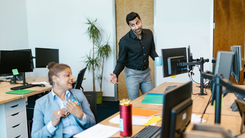 Two colleagues engaging in a cheerful conversation in a modern office setting
