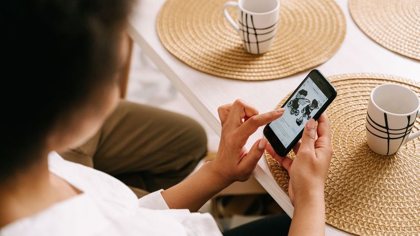 Woman browsing online store for baby stroller using smartphone at home