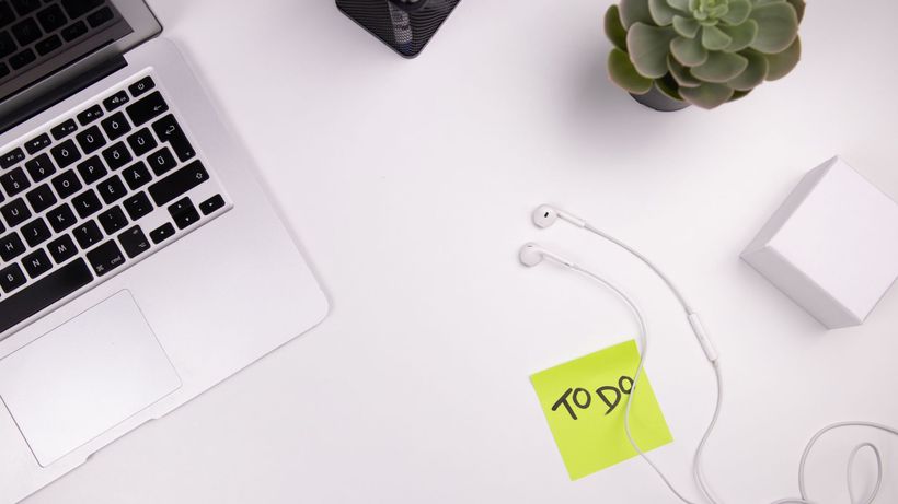 Organized workspace featuring a laptop, earphones, and a to-do list with plant decor