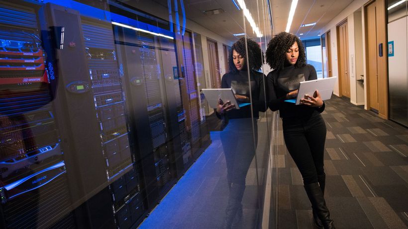 A woman using a laptop navigating a contemporary data center with mirrored servers