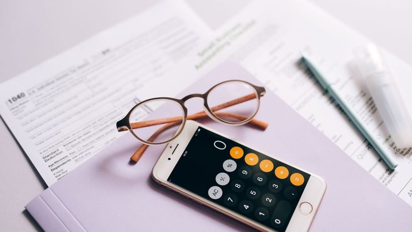 A smartphone calculator and glasses on tax documents, representing modern tax preparation