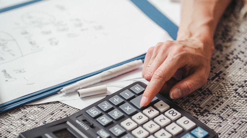 A hand using a calculator on top of documents, indicating financial calculation or analysis