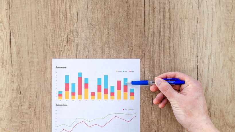 A hand points a pen at business graphs on a wooden table, highlighting data analysis