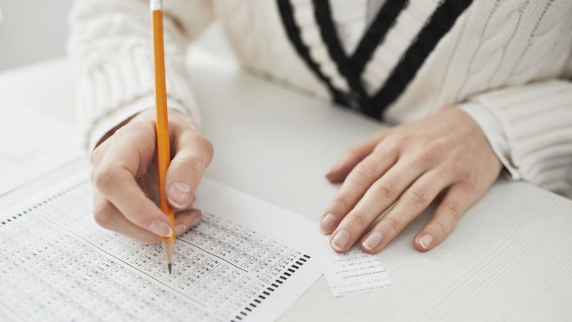 A student writing answers on a multiple-choice exam sheet at a desk