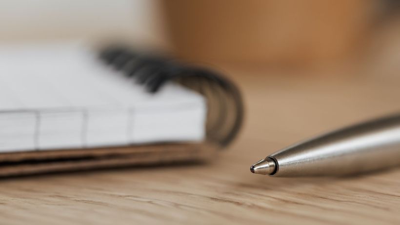 Side view closeup of opened ring bound notebook with blank pages near silver ball point pen placed on wooden table