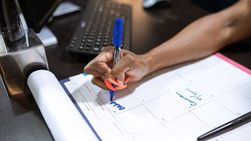 Detailed shot of a person's hand writing notes on a calendar using a blue marker