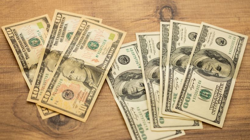 A collection of US dollar bills arranged on a wooden surface, showcasing currency denominations