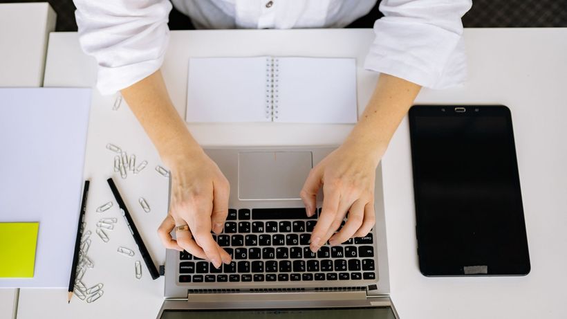 A workspace with a laptop, digital tablet, and hands typing, viewed from above