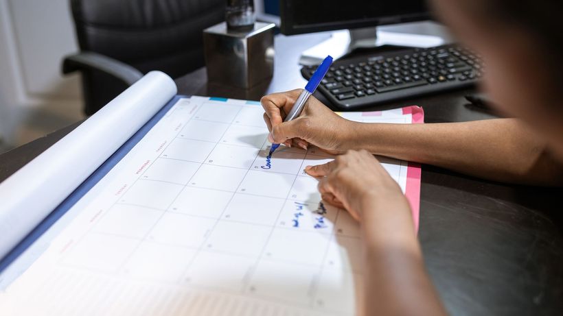 Close-up of a woman planning her schedule on a desk calendar in an office setting