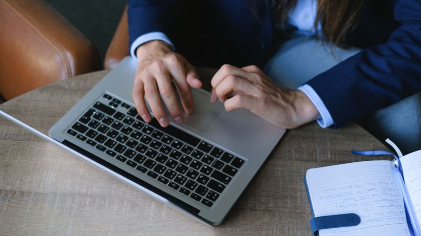 From above crop anonymous freelancer in stylish clothes sitting at table with opened notebook and working on project