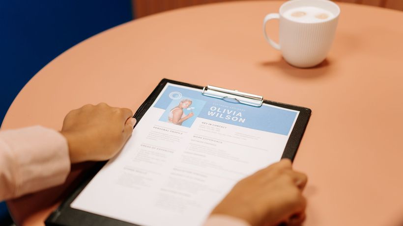 Close-up of hands holding resume during interview with coffee on table, highlighting workplace setting