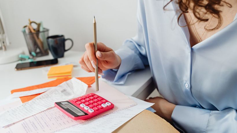 A woman is calculating expenses using a calculator and papers at her desk