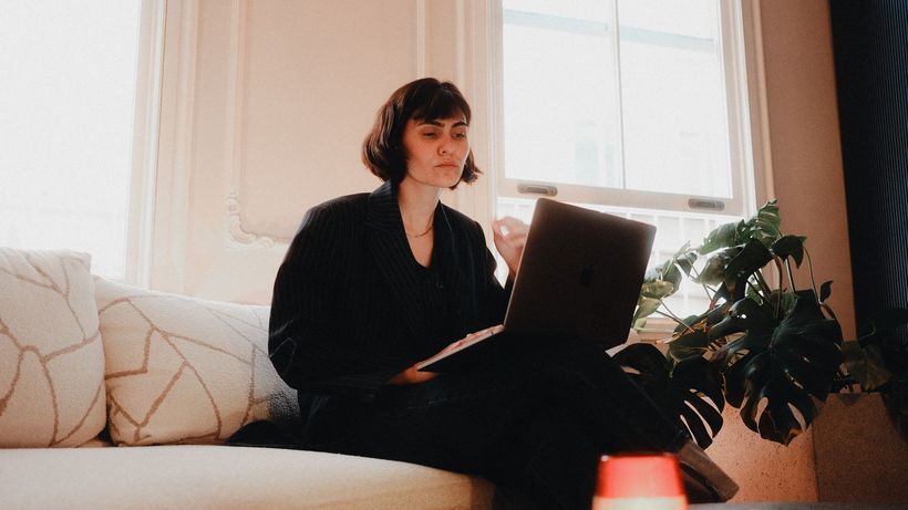 Woman in suit using laptop on sofa in bright room, modern lifestyle